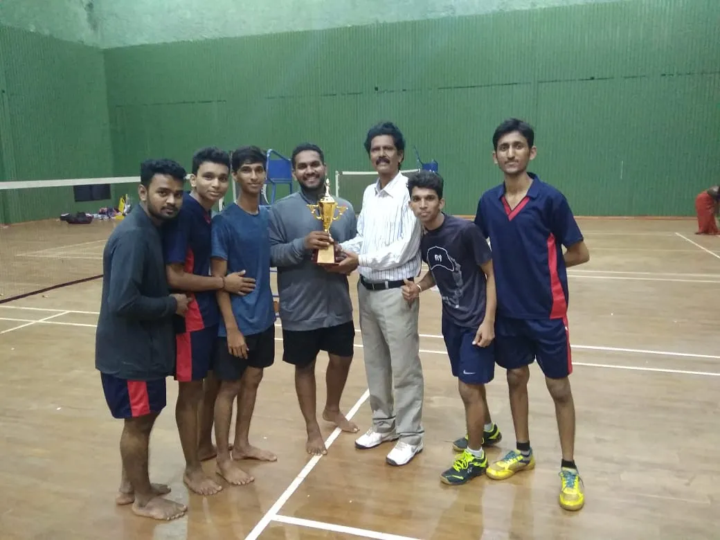 A BEC badminton team with their winners' trophy in the indoor court
